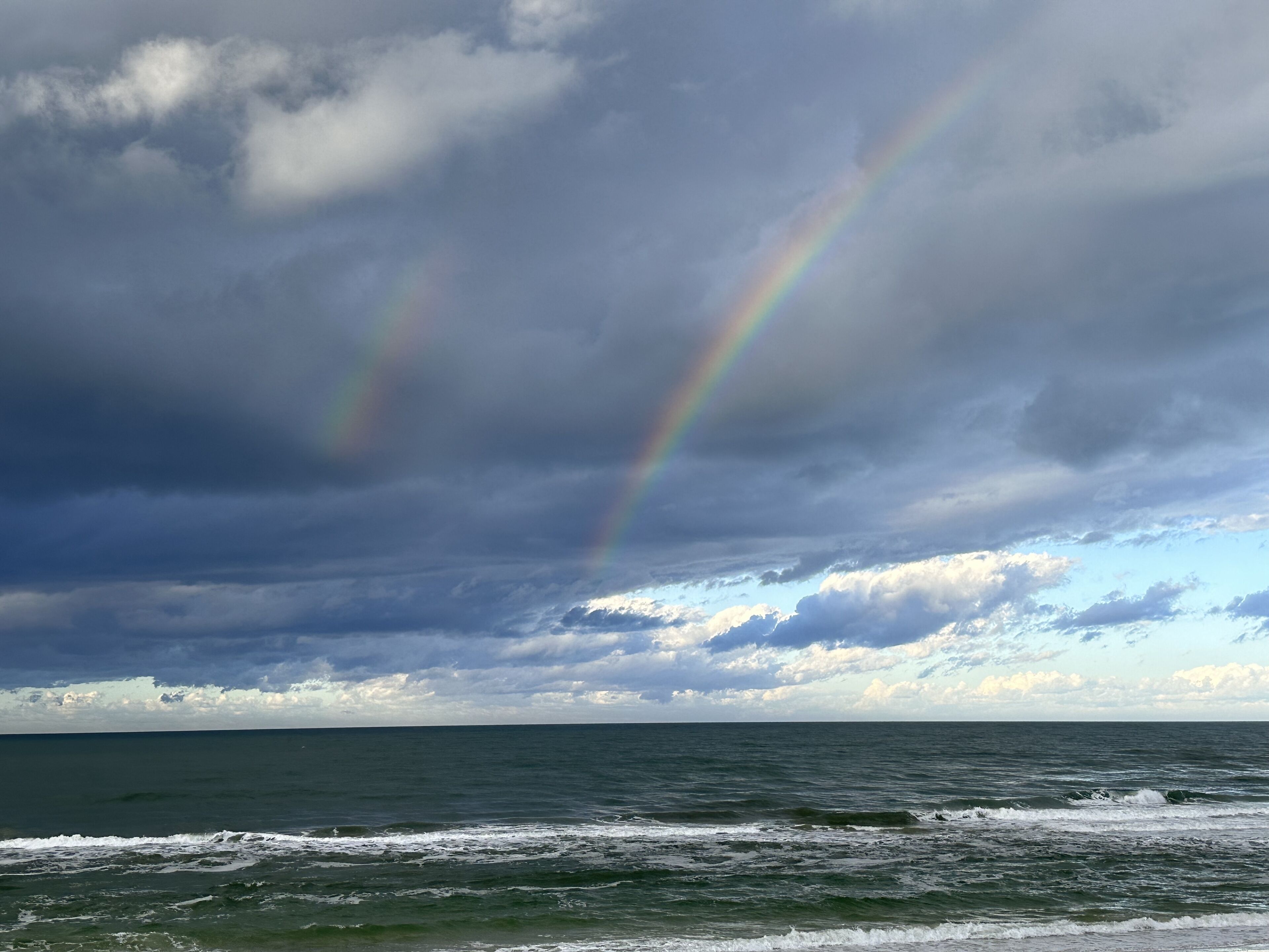 A beach with waves and a rainbow in the sky.