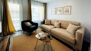 A living room with a sofa, a chair, a coffee table, and a rug. There are curtains on the windows, and three framed pictures on the wall. - Casa SoHo y Alex, Apartment 3B- 2 bedrooms (Estepona)