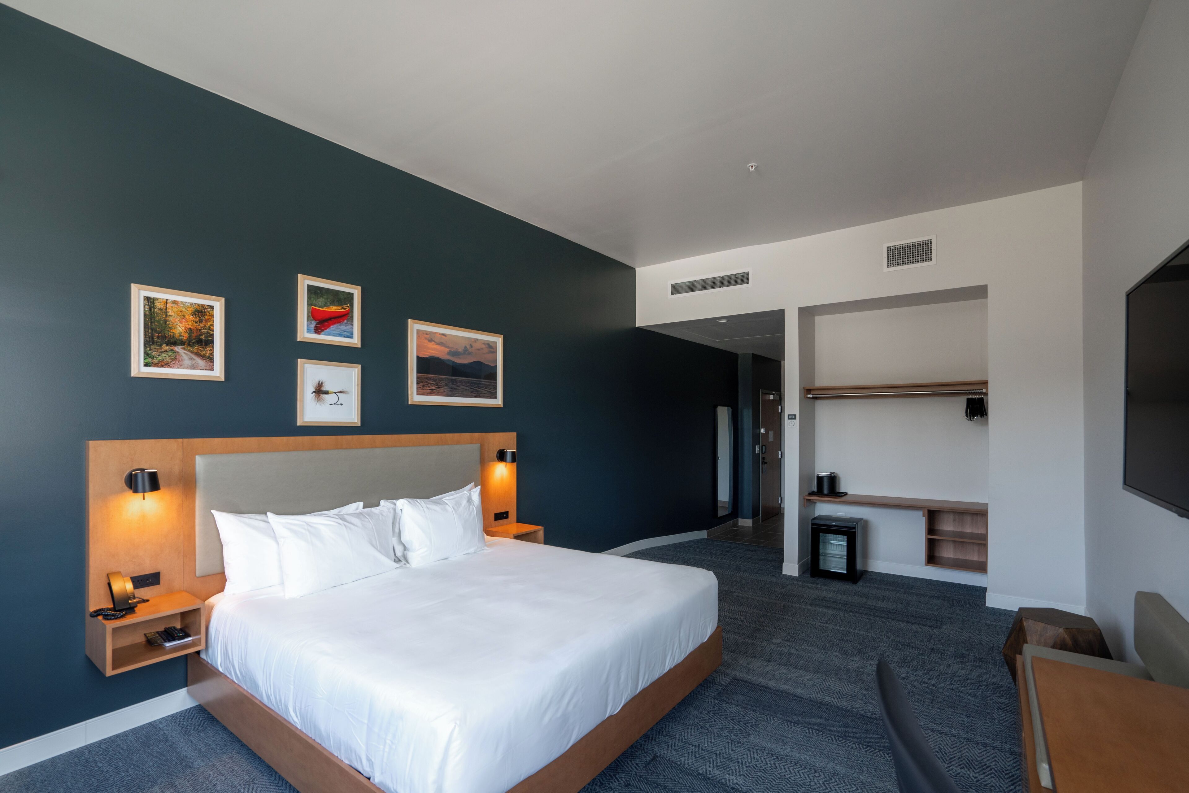 Une chambre d’hôtel moderne avec un grand lit, des tables de chevet, une télévision et des œuvres d’art accrochées au mur.