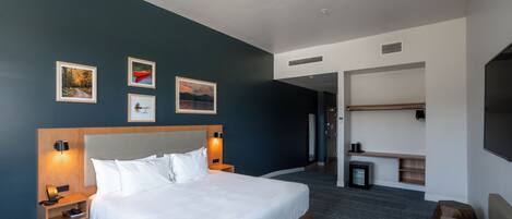 Une chambre d’hôtel moderne avec un grand lit, des tables de chevet, une télévision et des œuvres d’art accrochées au mur.