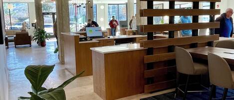 A modern reception area with a wooden partition, a reception desk, and a seating area with a potted plant.