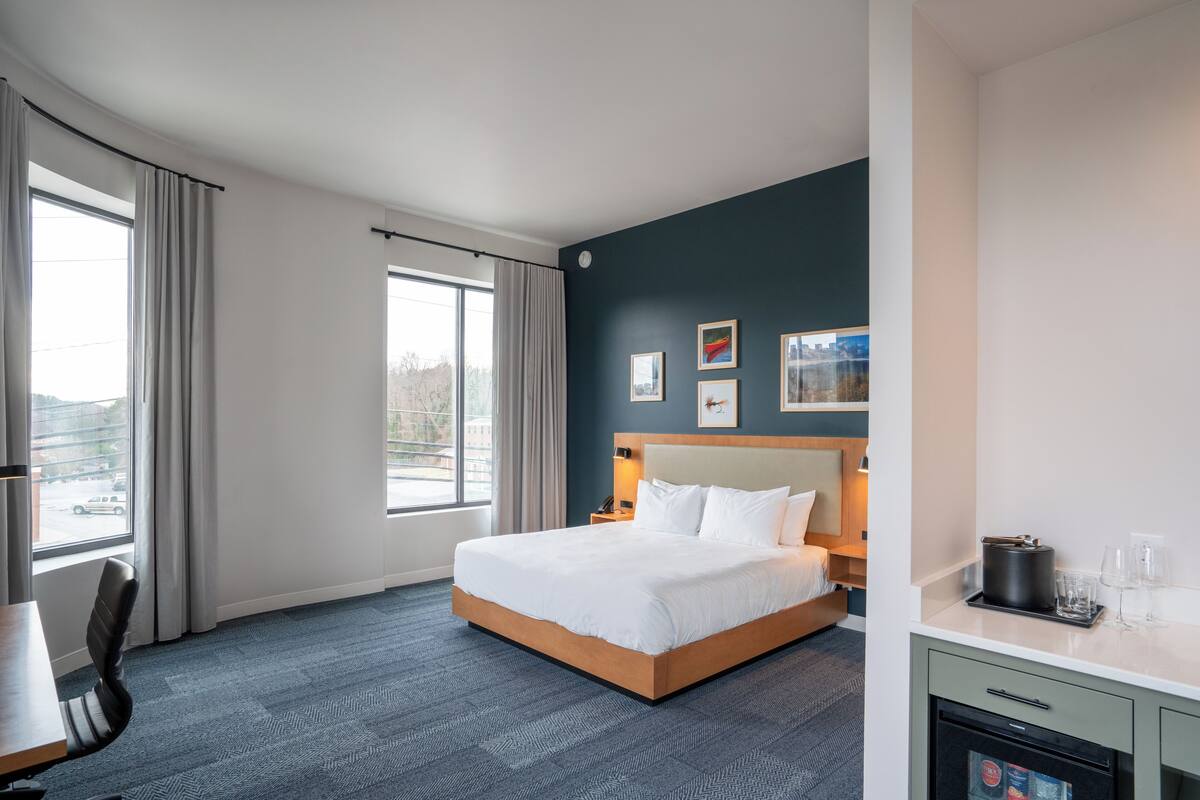 A modern hotel room with a large bed, a desk, and a view of the city.