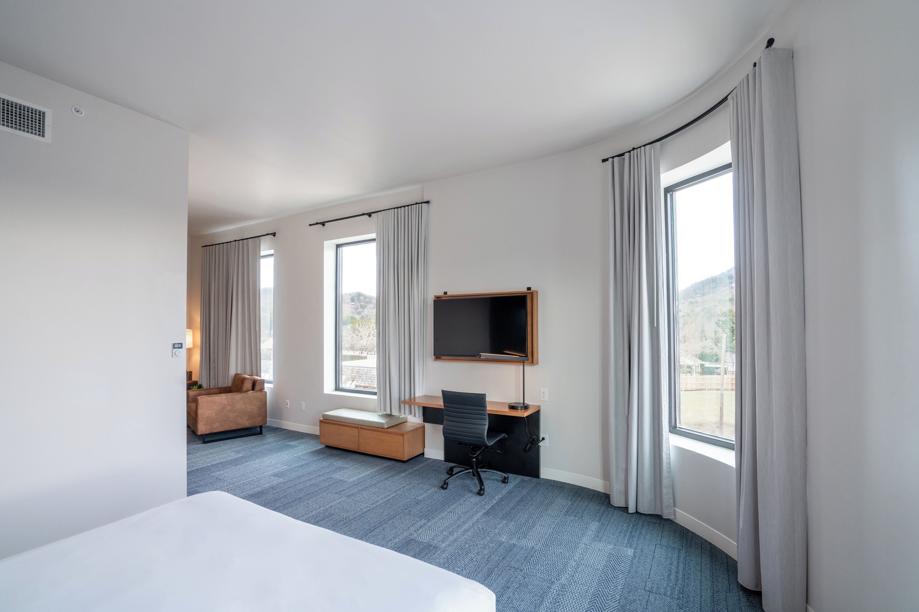 Une chambre d’hôtel équipée d’un lit, d’un bureau, d’une chaise, d’une télévision et de grandes fenêtres.