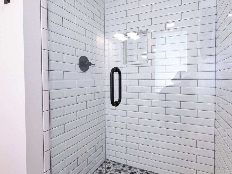 A glass-enclosed shower with white subway tiles and a pebble-patterned floor.