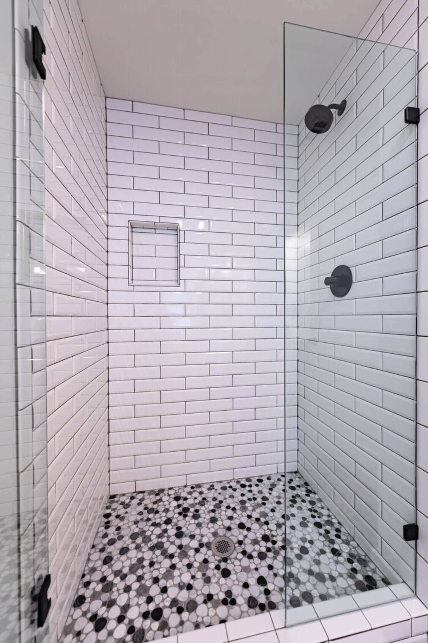 A glass-enclosed shower with white subway tiles and a speckled floor.