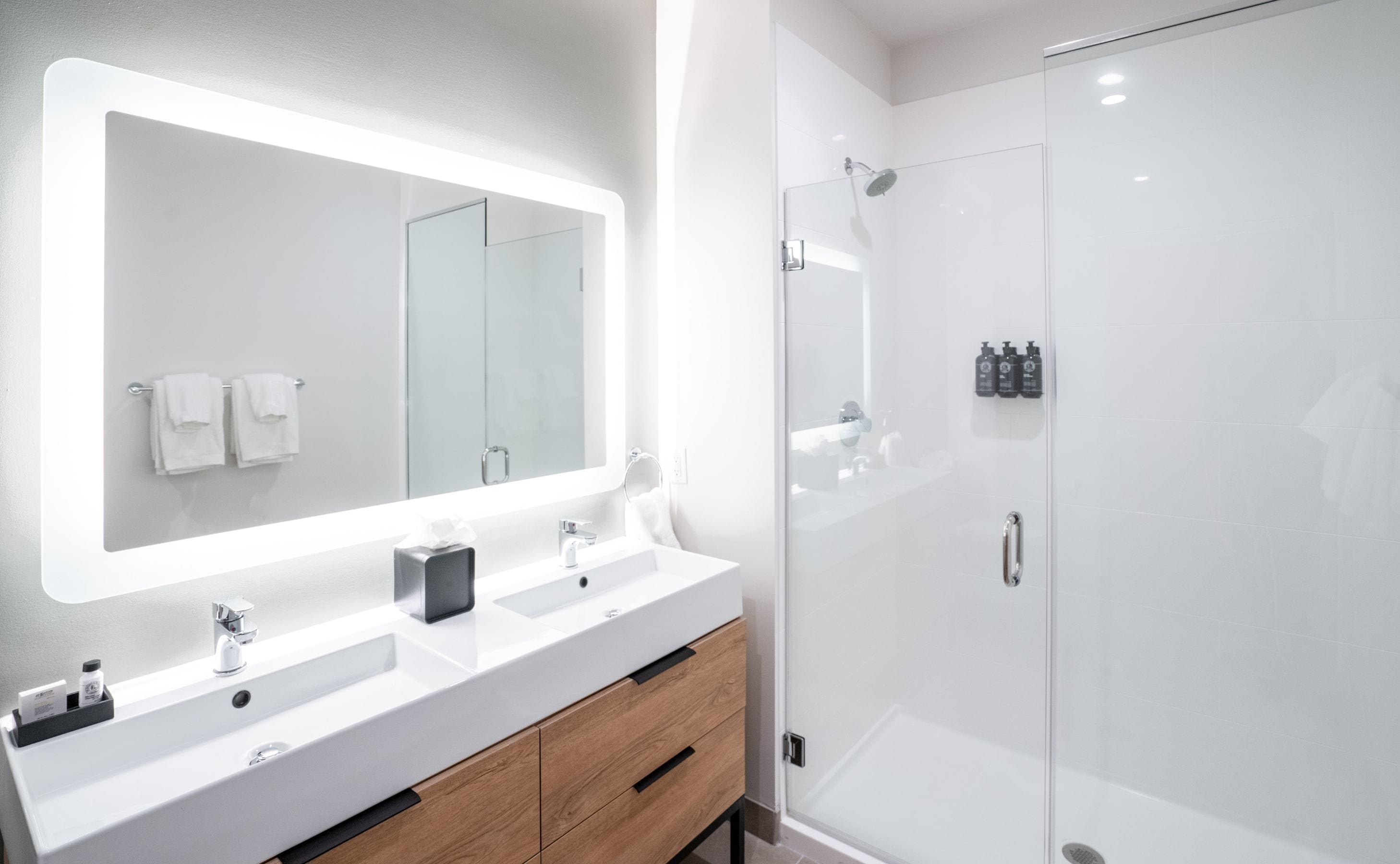 Une salle de bain moderne avec un grand miroir, deux vasques, un meuble en bois et une douche à parois de verre.