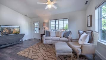 A spacious living room with a large sectional sofa, a chaise lounge, a wooden entertainment unit, and a large window providing natural light.