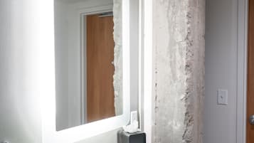 A bathroom with a white sink, a large mirror, and a rough-textured wall.