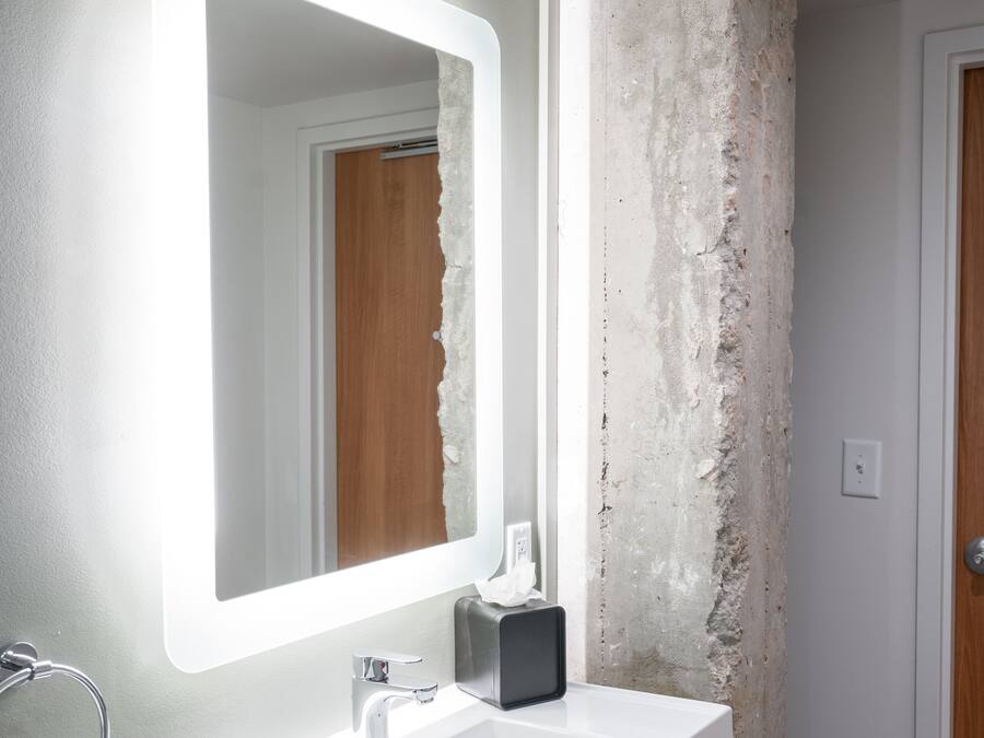 A bathroom with a white sink, a large mirror, and a rough-textured wall.