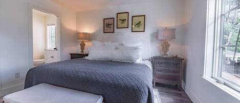 Een slaapkamer met een groot bed, nachtkastjes, een bankje en ingelijste foto's aan de muur.