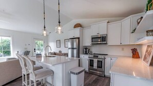 A modern kitchen with white cabinetry, stainless steel appliances, and a central island with bar stools. - Bridge Creek Inn (Clayton)