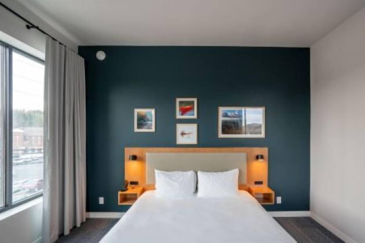 A hotel room with a large bed, a dark blue accent wall, and three framed pictures.