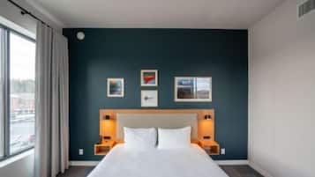 Una habitación de hotel con una cama grande, una pared de acento azul oscuro y tres cuadros enmarcados.