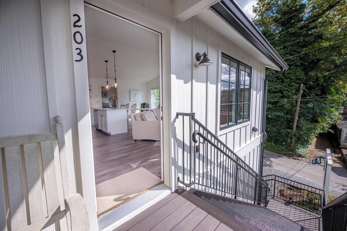 A two-story house with a visible number '203' on the exterior wall, a staircase leading to the upper floor, and a small porch area.