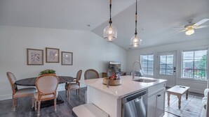 A modern kitchen with a central island, dining area with chairs, and large windows. - Bridge Creek Inn (Clayton)