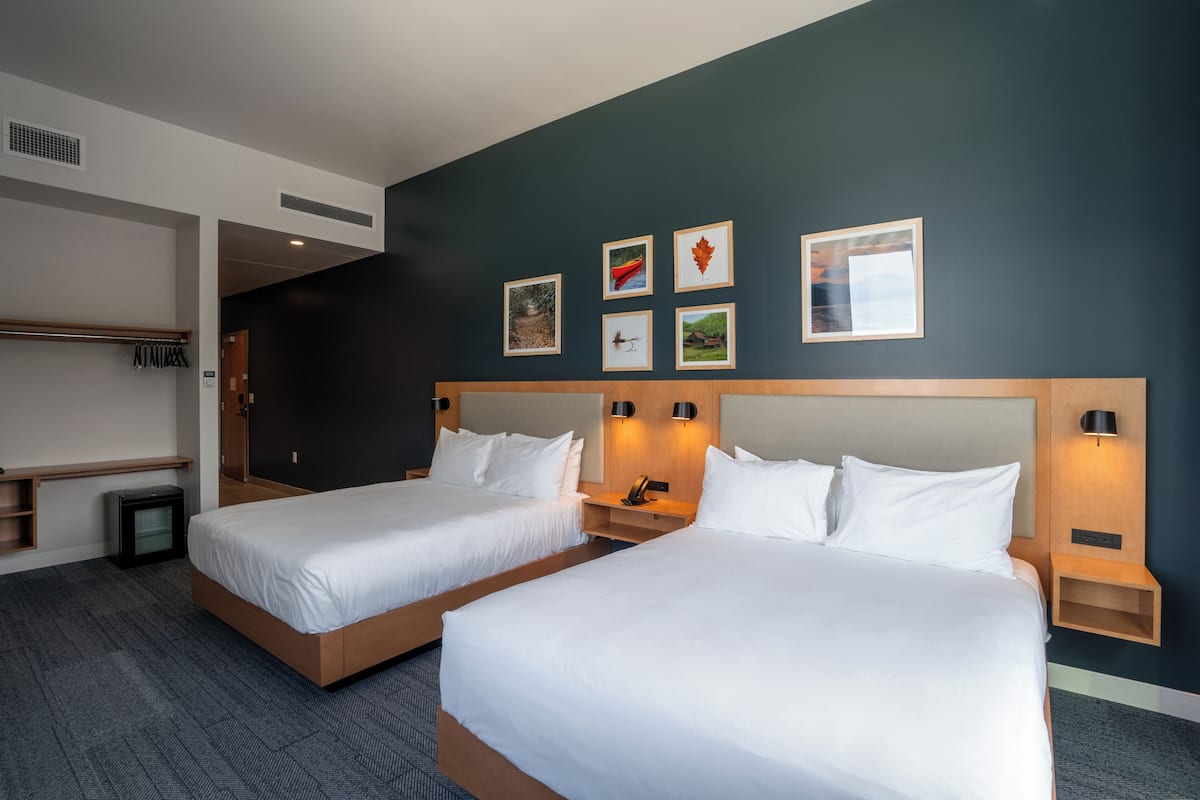A hotel room with two beds, a wardrobe, a small desk, and a wall with framed pictures.