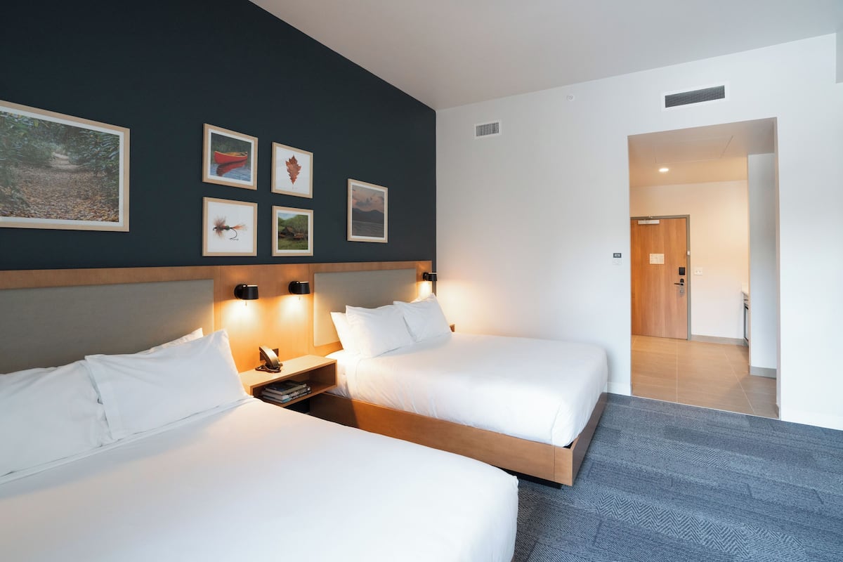 A hotel room with two beds, a nightstand, a wall-mounted lamp, and framed pictures.