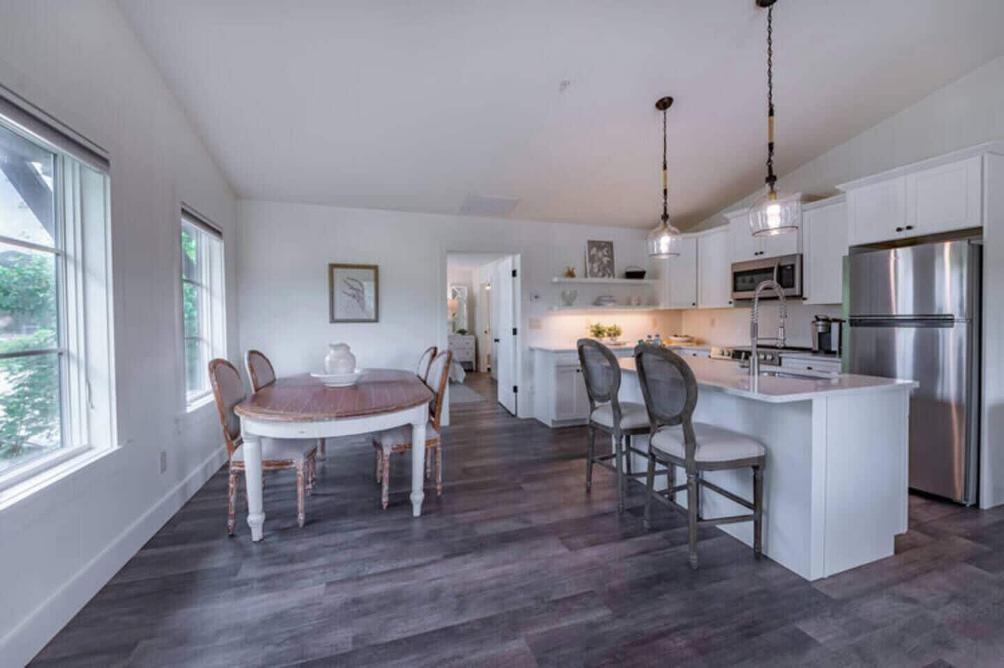 A modern kitchen with white cabinetry, a stainless steel refrigerator, and a dining area with a wooden table and chairs.