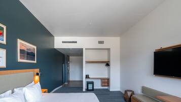 Una habitación de hotel moderna con cama, zona de estar, televisor y un pequeño escritorio.