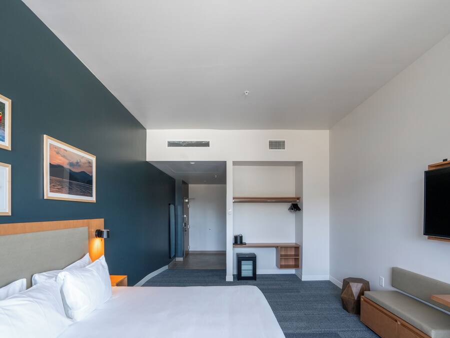 Una habitación de hotel moderna con cama, zona de estar, televisor y un pequeño escritorio.