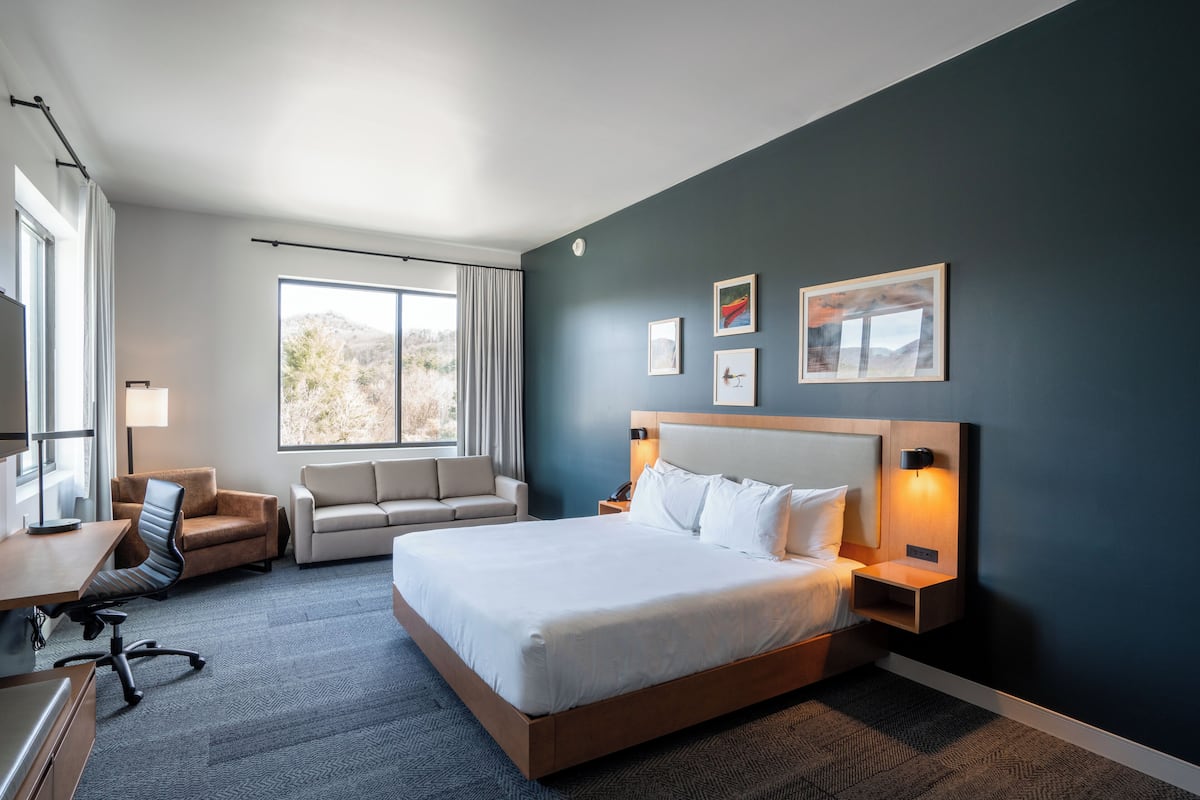 A modern hotel room with a large bed, a desk, a chair, and a sofa.