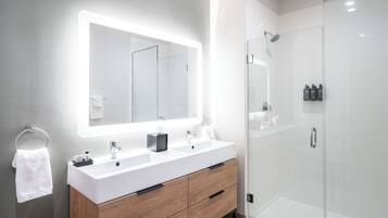 Un baño moderno con un espejo grande, dos lavamanos, un mueble de tocador con cajones y una cabina de ducha de vidrio.