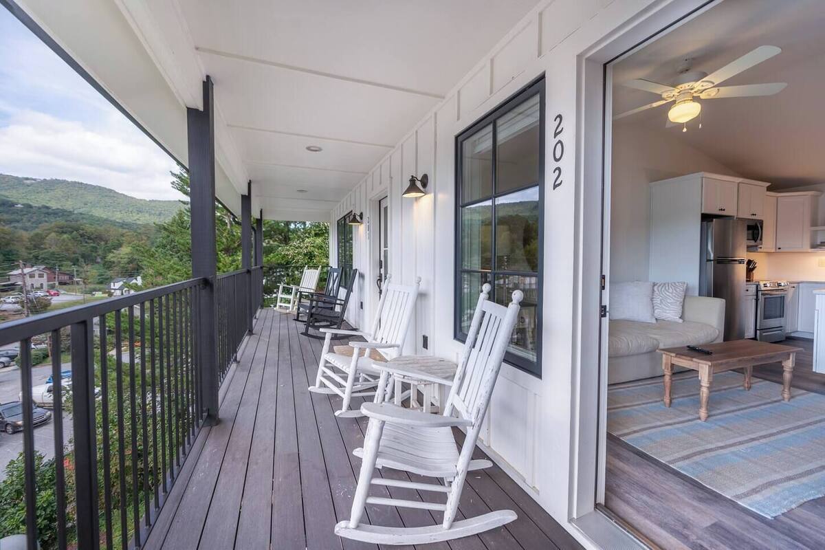 A balcony with white rocking chairs, a view of the landscape, and a kitchen area with cabinets and appliances.
