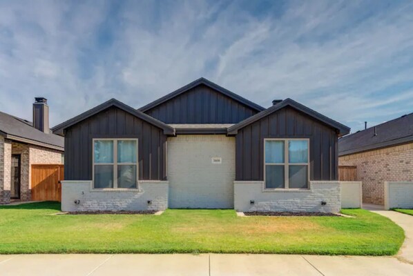 Symmetrical two-story house with a central garage door and two side entrances, set amidst a well-maintained lawn and paved driveway.