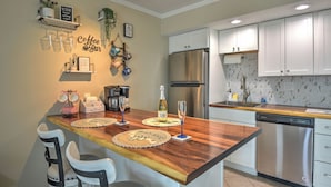 A kitchen with a wooden island, white cabinets, stainless steel appliances, and a coffee bar setup.