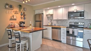 A modern kitchen with white cabinets, stainless steel appliances, and a wooden island with bar stools.