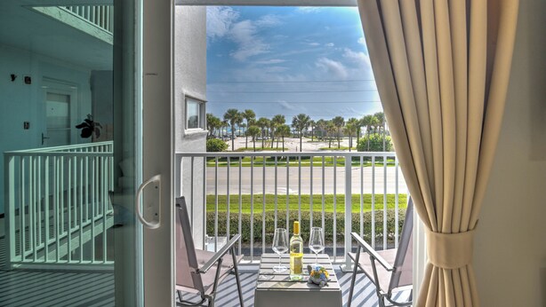 A balcony with a table set for two, overlooking a beach and palm trees.