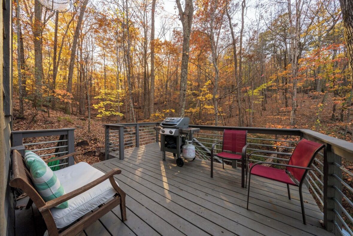 A wooden deck with a grill, red and green chairs, and a bench.