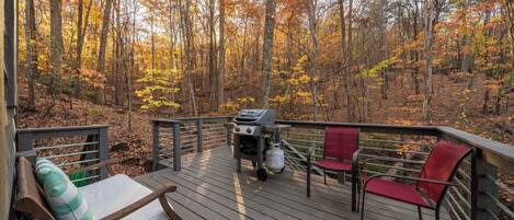 A wooden deck with a grill, red and green chairs, and a bench.