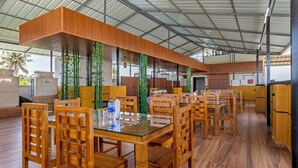 A restaurant with wooden tables and chairs, a high ceiling, and a view of the outdoors. - Treebo Vsaffron Regency, Punnamada Lake (Ambalapuzha)