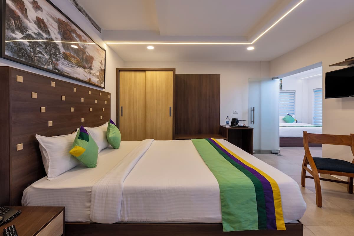 Habitación de hotel con una cama grande, cabecera de madera, un cuadro en la pared, televisor montado y una silla.