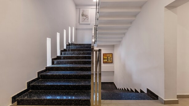 A modern staircase with black marble steps and a glass railing, leading to a landing with a framed artwork. - Treebo Vsaffron Regency, Punnamada Lake (Ambalapuzha)