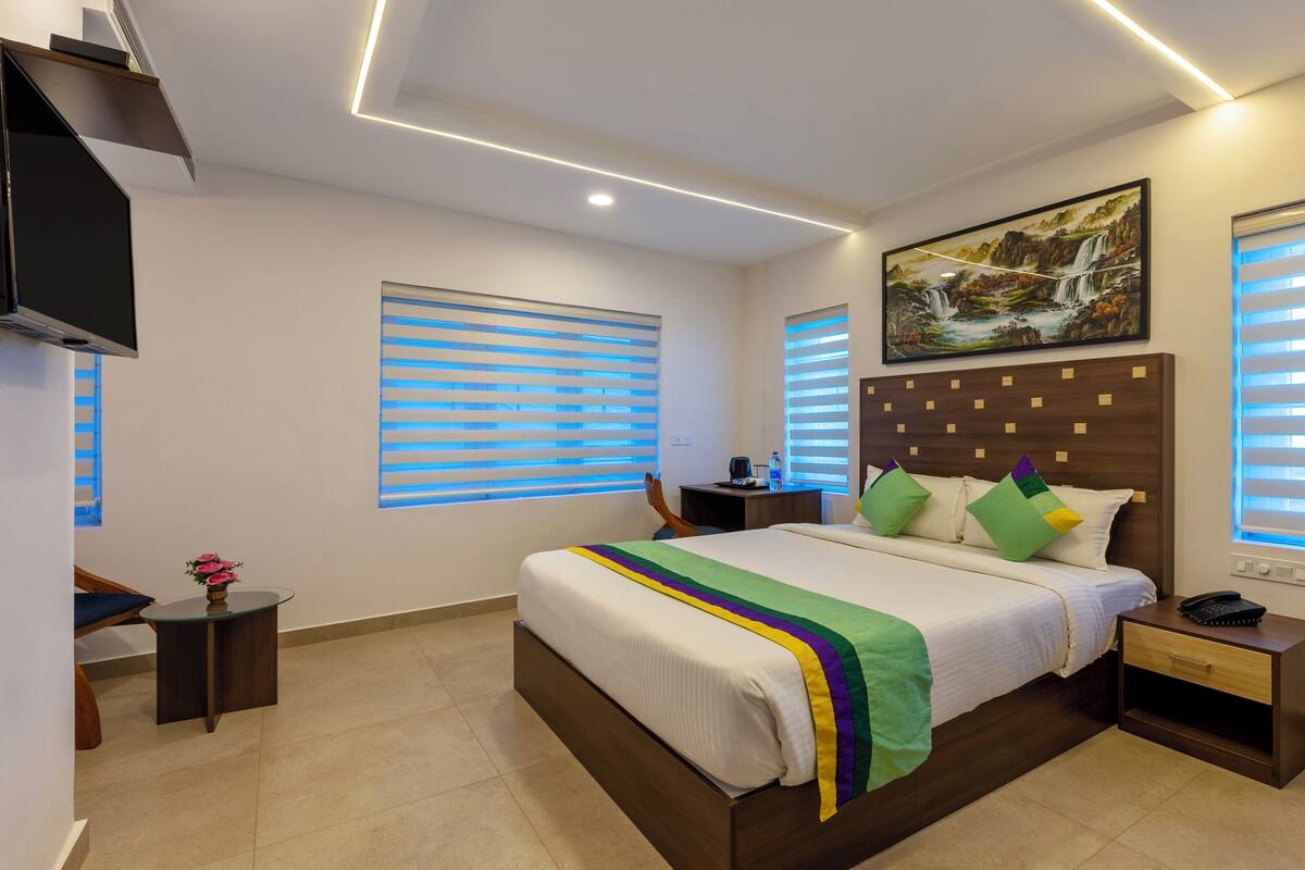 Una habitación de hotel moderna con una cama grande, un escritorio, una silla, un televisor y un cuadro en la pared.