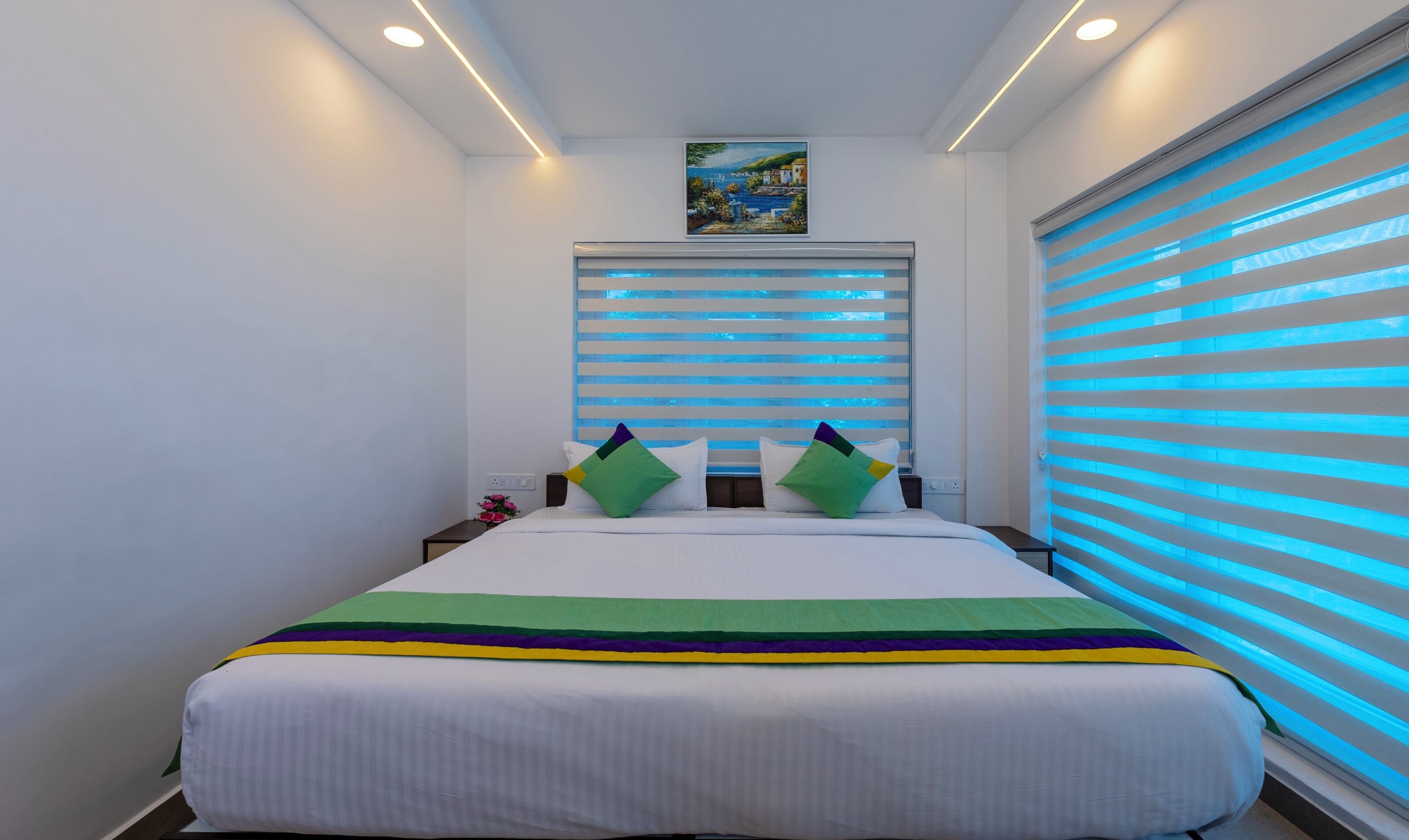 A modern bedroom with a large bed, striped blinds, and a painting above the bed.