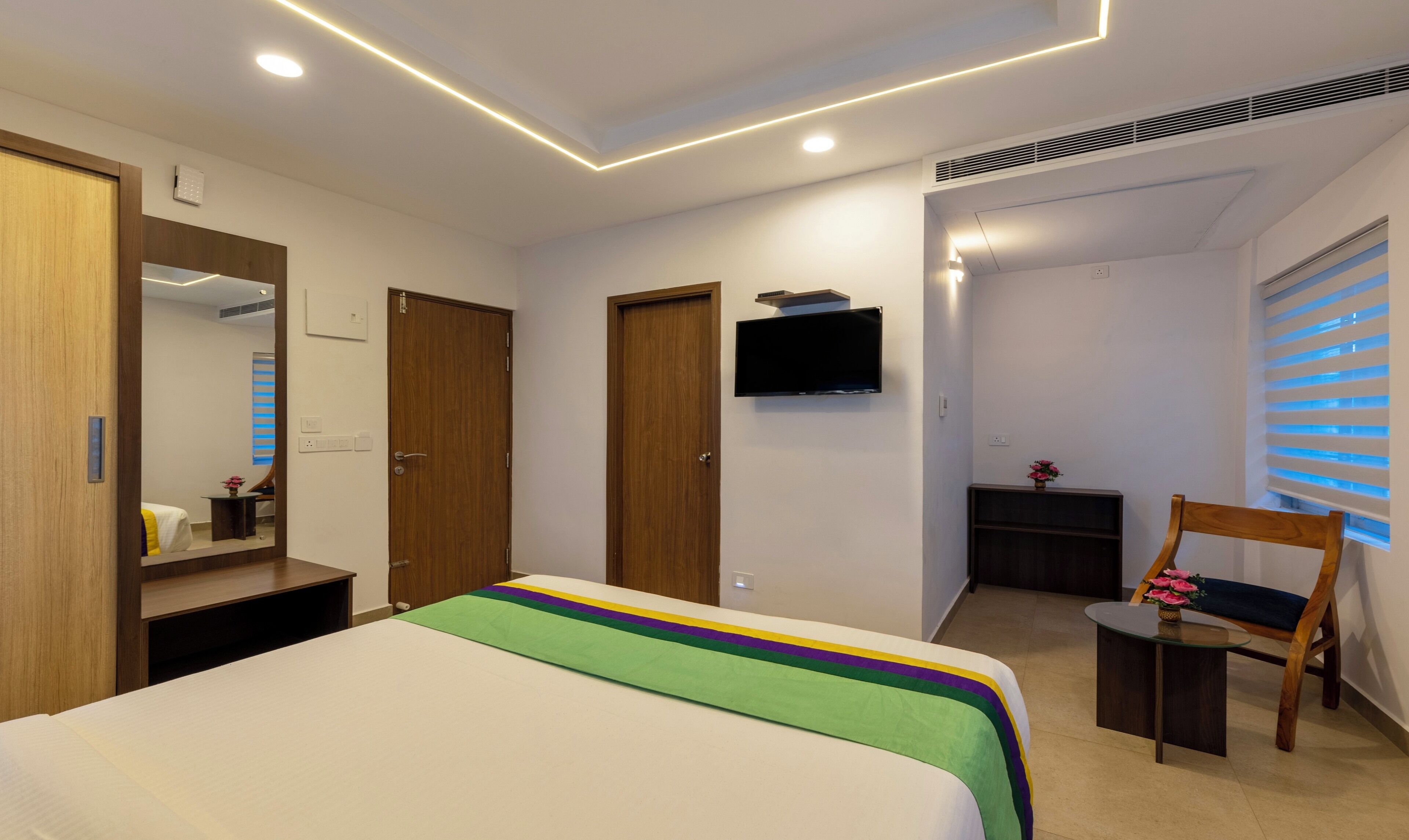 A modern hotel room with a large bed, a TV mounted on the wall, a desk, and a chair.