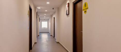 A long, narrow hallway with doors on both sides, a window at the end, and a yellow sign on the right wall.