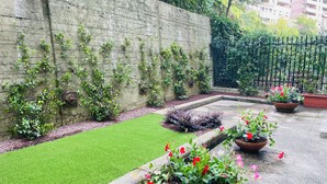 Un jardín con césped verde, plantas en macetas y un muro de hormigón.