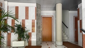Un vestíbulo moderno con una pared de mármol, una puerta de madera, una columna blanca y una escalera.