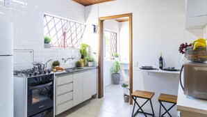Moderni keittiö, jossa on valkoiset kaapit, kaasuliesi ja sisäänrakennettu uuni. Siellä on myös ruukkukasveja ja pieni ruokailutila, jossa on pöytä ja tuolit.