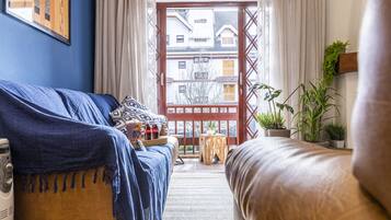 Ein Zimmer mit einem blauen Sofa, einem braunen Sofa, einem Holztisch mit Tablett und Blick auf traditionelle Gebäude durch ein hölzernes Tor.