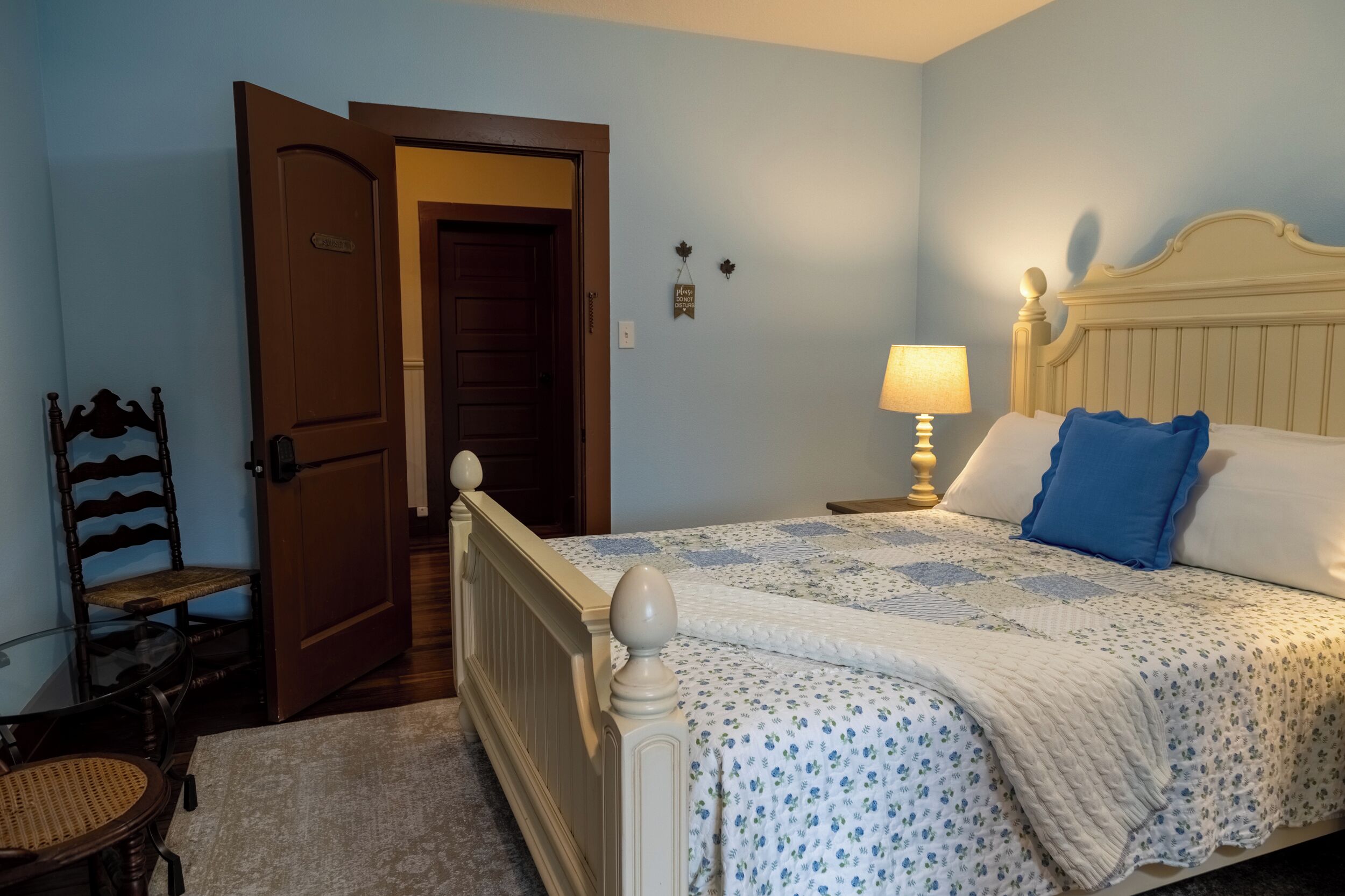 Quarto com cama, poltrona, mesa de cabeceira e porta.