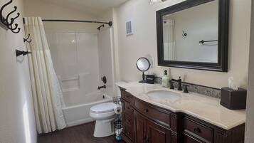 A bathroom with a bathtub, toilet, vanity with a mirror, and a shower curtain.