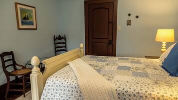A bedroom with a bed, a chair, a door, a painting, and a lamp.