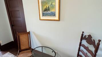 Une pièce avec une porte marron, un tableau encadré représentant un paysage, deux chaises en bois et une petite table en verre.