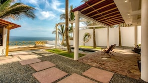 Un espacio al aire libre techado con piscina, palmeras y vista al océano.