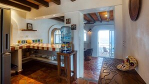 Una cocina con un gran dispensador de agua, techo de madera rústica y suelo de piedra.